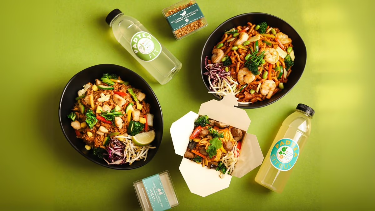 Wok noodles in black bowls and a takeaway box, with lemonades, on a green background, from above