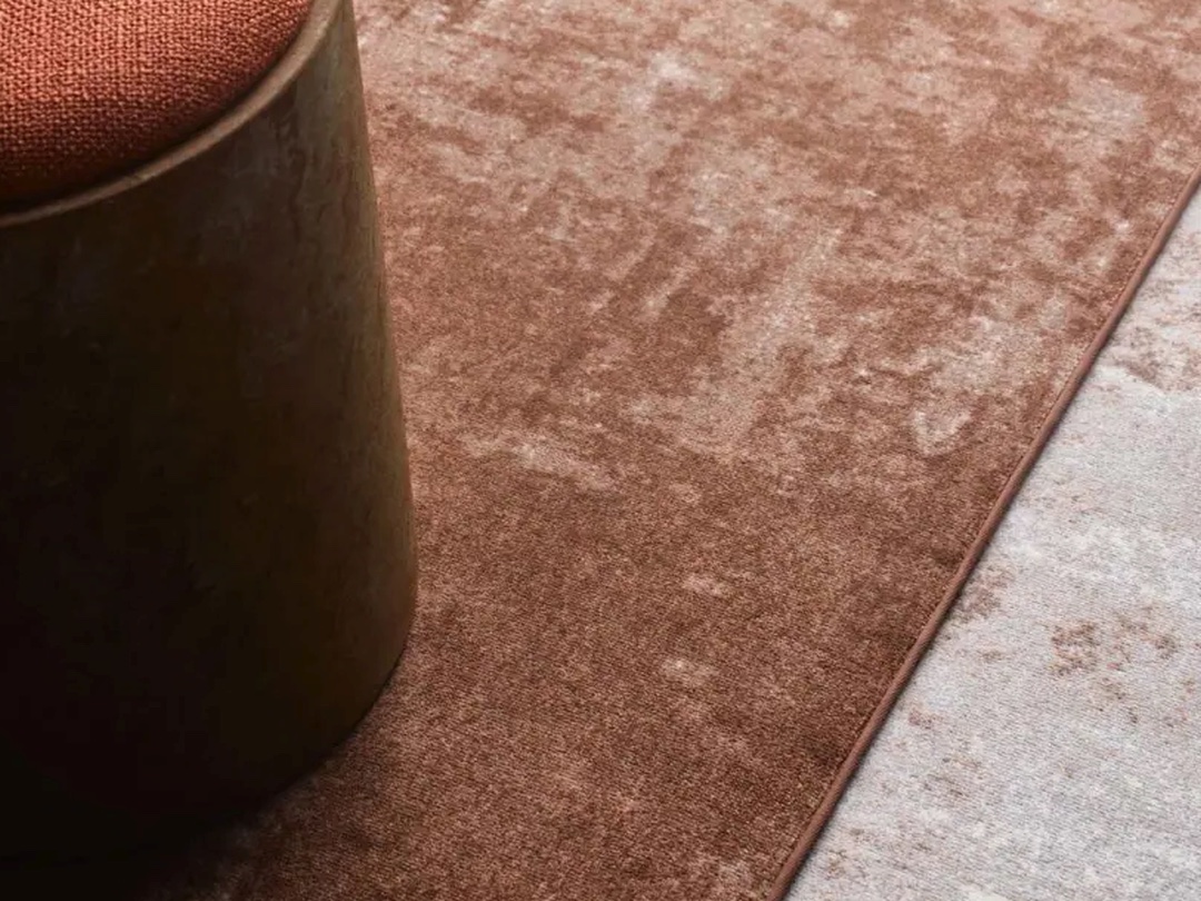 Close-up of rust-brown and light grey carpet next to a wooden seat