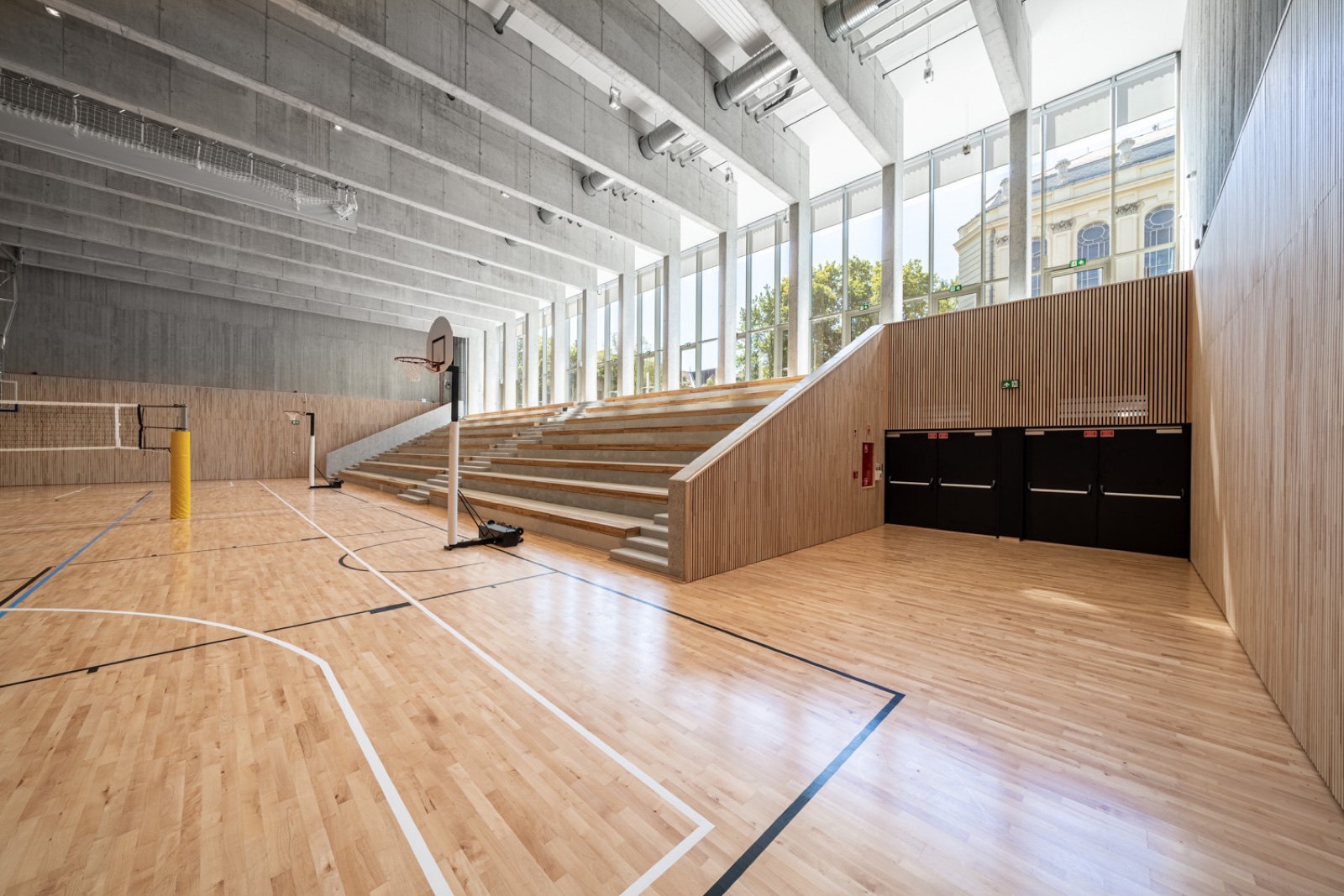 Wood-floored sports hall with a basketball hoop and stands